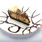 A slice of peanut butter chocolate cake on a white plate from Genova's To Go. Delectable delight