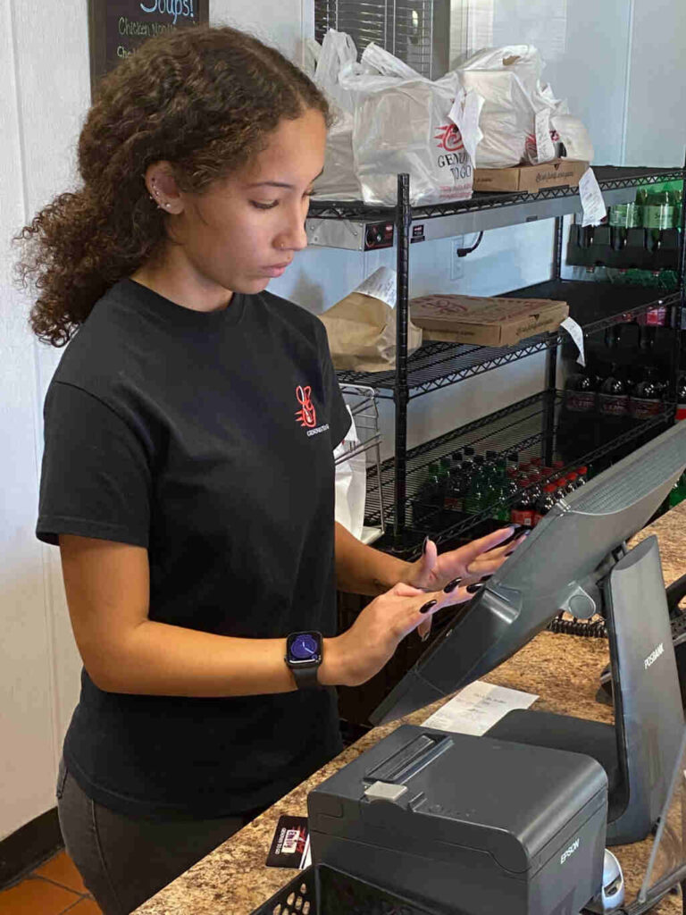 A woman in a black shirt using a tablet - Genova's To Go front end worker multitasking efficiently.