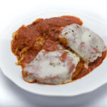 Plate of Chicken Parm meatballs and sauce on white surface. Delicious Italian dish from Genova's To Go.
