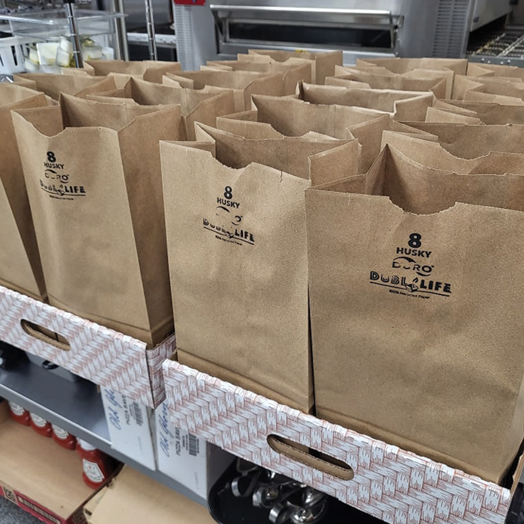 Enjoy these bagged lunches prepared by Genova's To Go. including a sandwich, a drink, and a bag of chips.